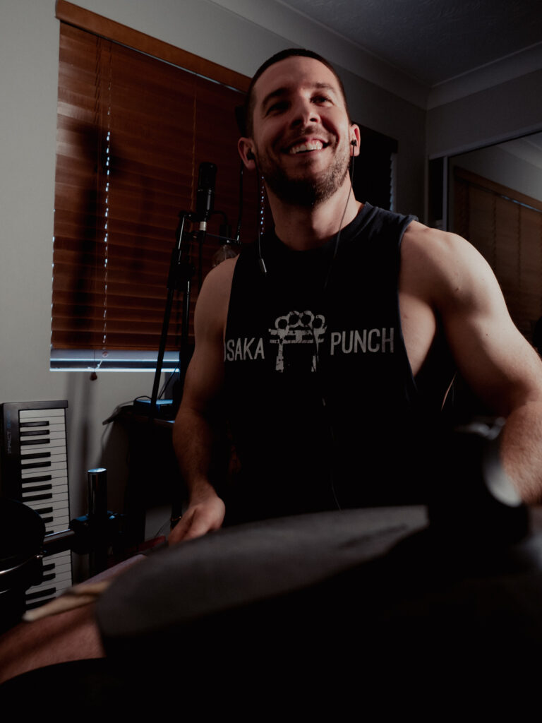 Matt from Keen Physique smiling and drumming on an electric drum kit.