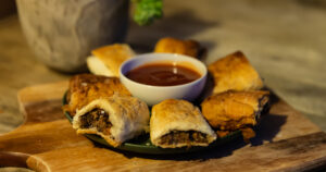 An image with a plate holding vegan sausage rolls and tomato sauce.