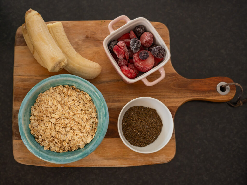 Picture of all the smoothie ingredients laid out on a cutting board, including bananas, mixed berries, oats, and the seed mix.